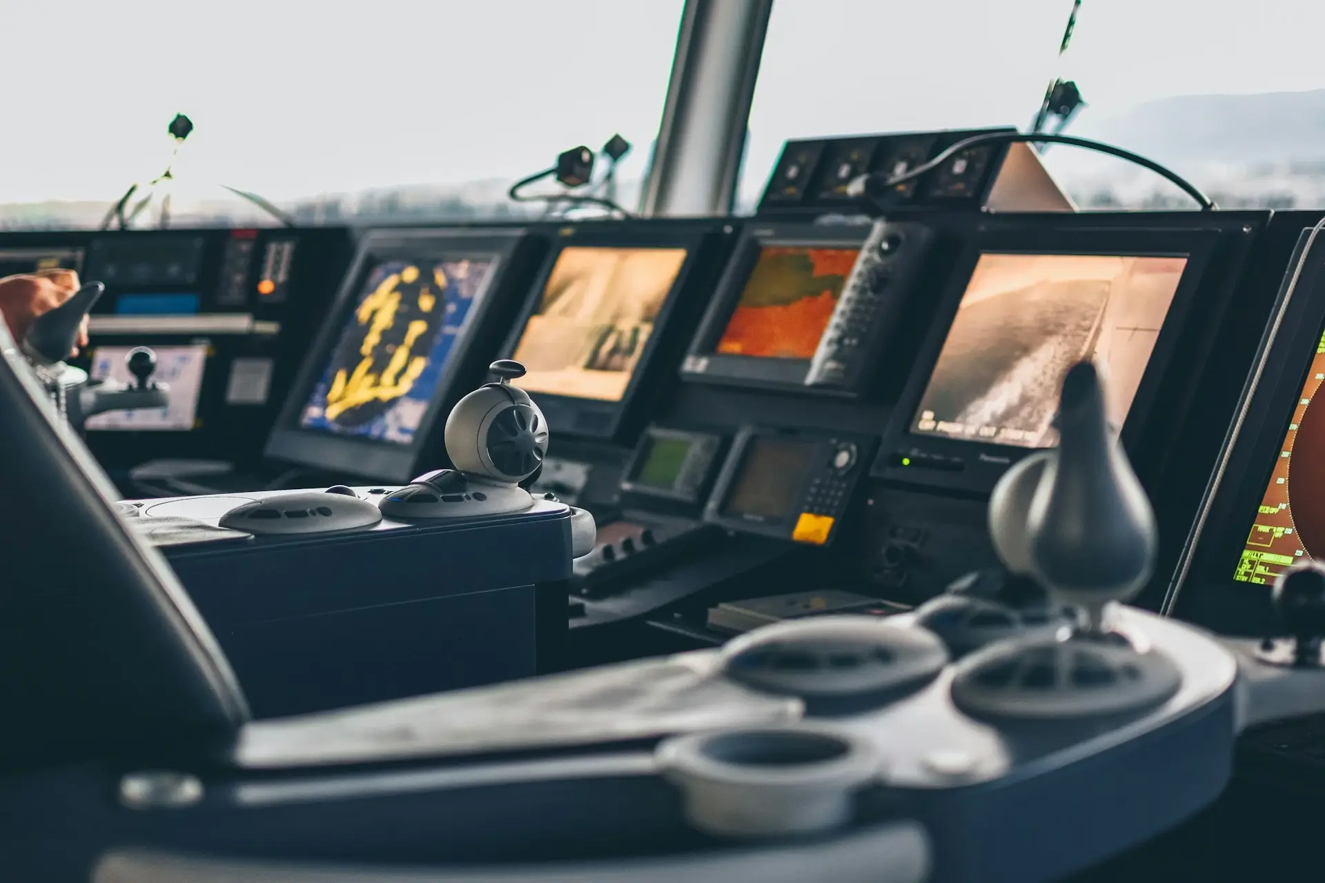 Kokpit nowoczesnego statku przedstawiający szereg elektronicznych paneli nawigacyjnych i kontrolnych z różnymi ekranami, pokrętłami i mechanizmami sterującymi.