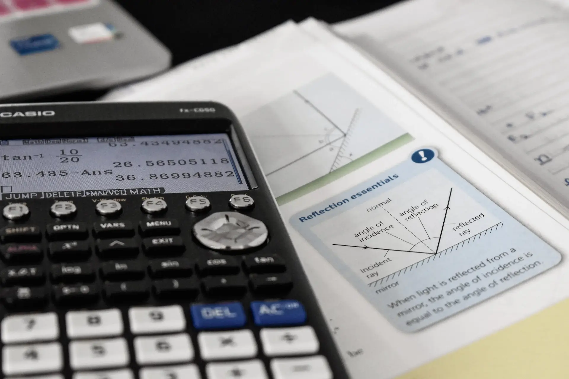 Kalkulator naukowy wyświetlający na ekranie obliczenia trygonometryczne, z formułami wydrukowanymi na arkuszu roboczym w tle, co wskazuje na środowisko do nauki.